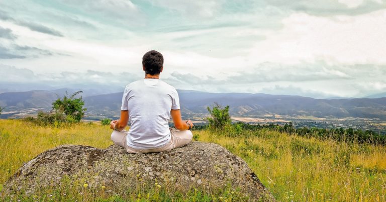 Hombre sentado en una piedra está meditando en la naturaleza