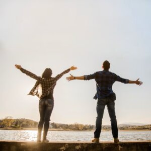 Une femme de dos à côté d'un homme de dos, les deux face à la mer avec les bras ouverts