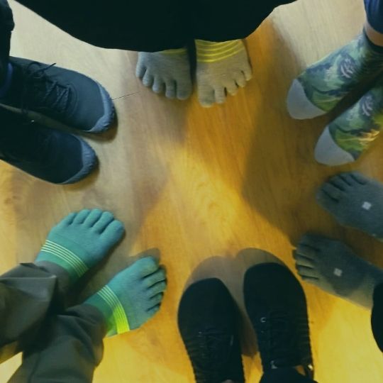 Grupo de personas en círculo practicando descalzas, con calcetines de dedos o calzado barefoot, en una clase de Chikung centrada en los pies.